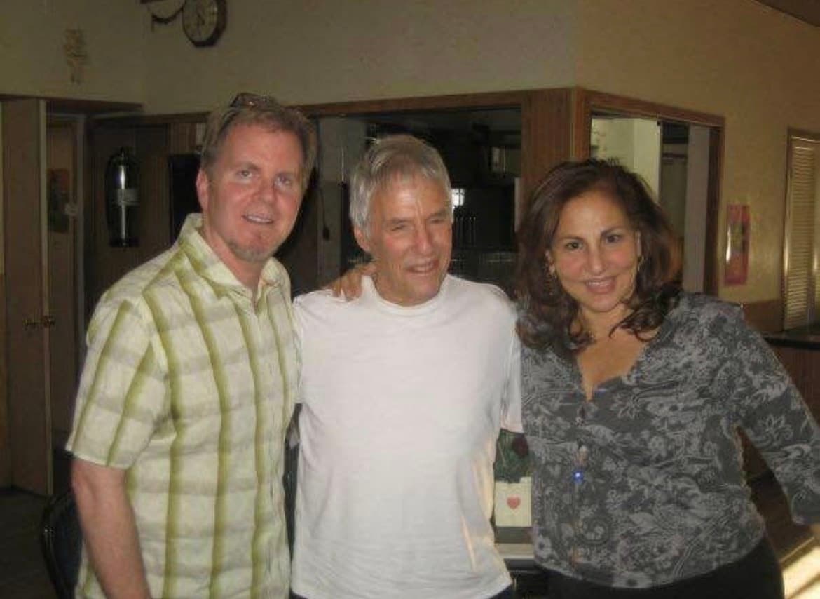 Steve Gunderson, Burt Bacharach and director Kathy Najimy standing together, smiling, in a wood-panelled room.