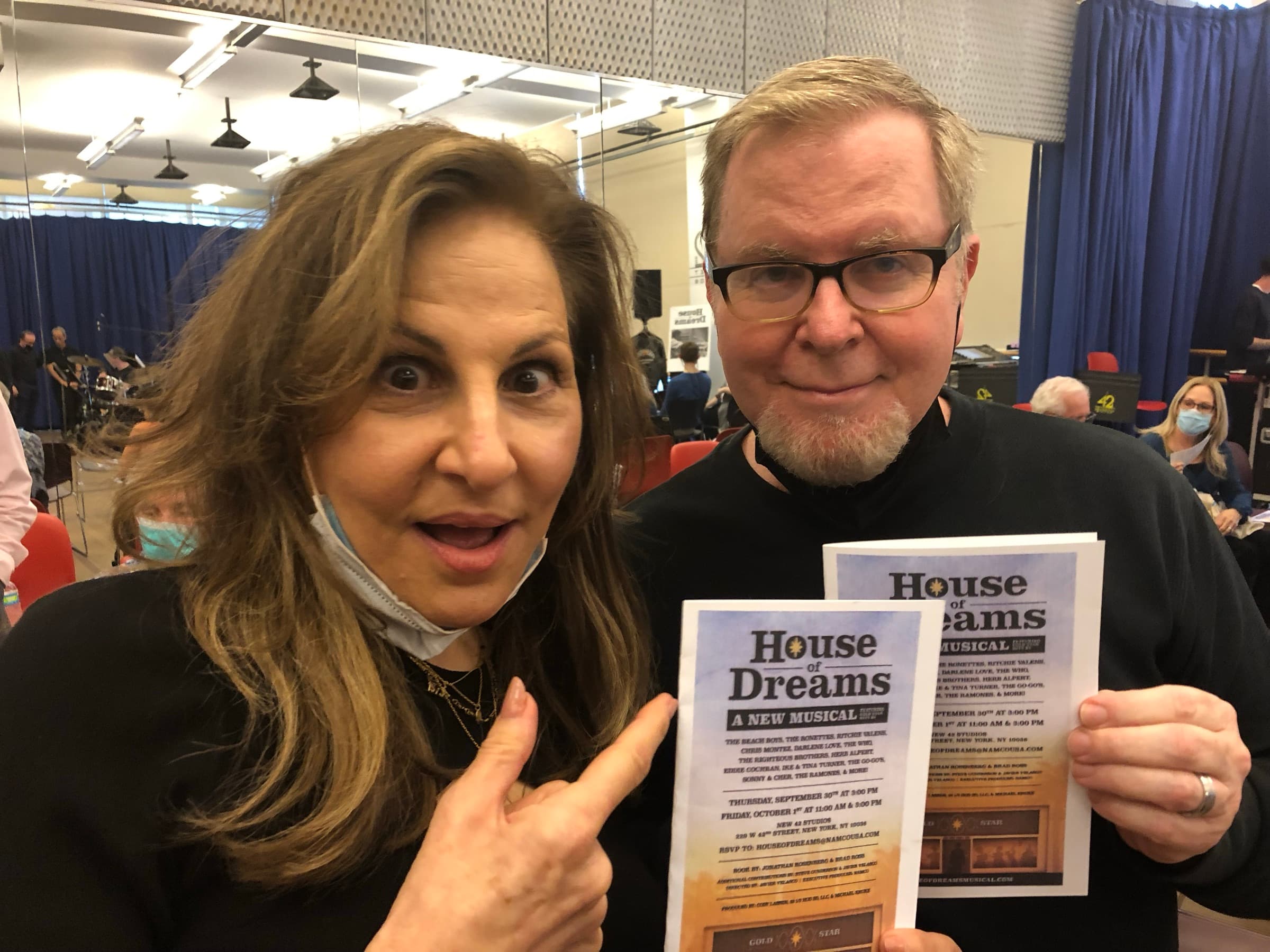 Steve Gunderson and Kathy Najimy hold up House of Dreams workshop programs in a rehearsal studio, with a band setting up behind them.